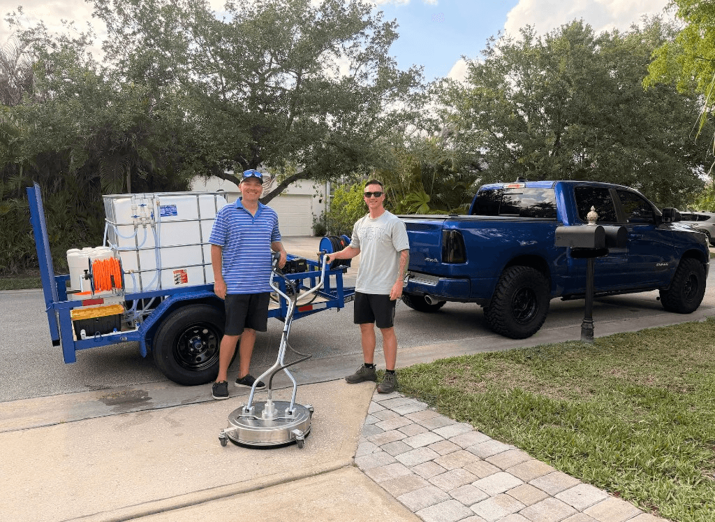 Crew with blue Ram truck, pressure washing trailer, and surface cleaner on a residential driveway